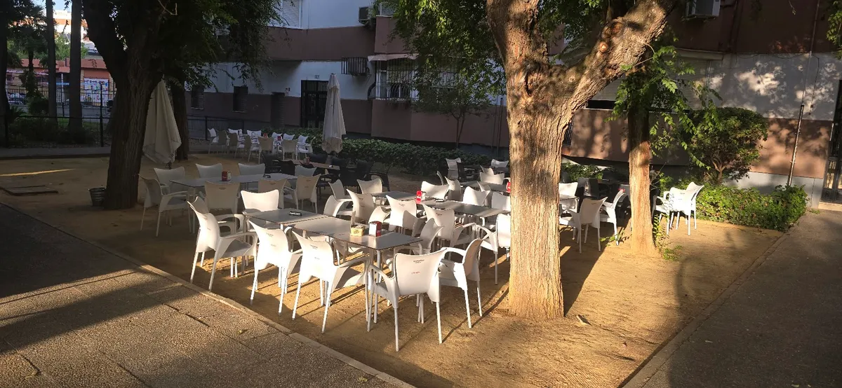 La terraza de El Fogón de Chela, con veladores y mesas a la sombra de los árboles